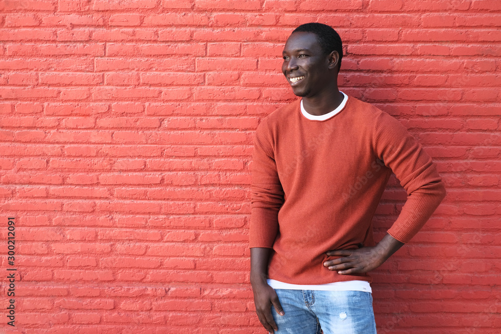 African Young Man Smiling And Leaning On Red Wall African Young Man Smiling And Leaning On Red Wall