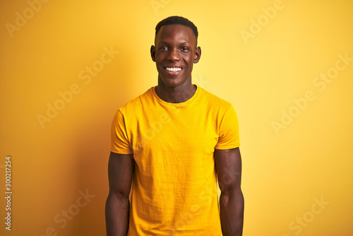 Young african american man wearing casual t-shirt standing over isolated yellow background with a happy and cool smile on face. Lucky person.