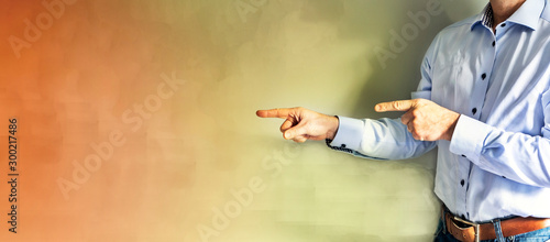 The man points with his index finger to the place to copy. A man in a blue jeans shirt and a leather belt. Bright yellow and orange wall.