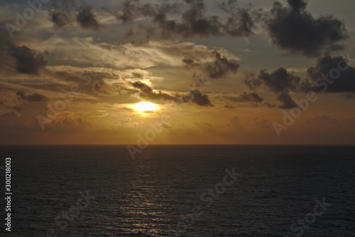 Yellow orange sunset above ocean and dramatic clouds.