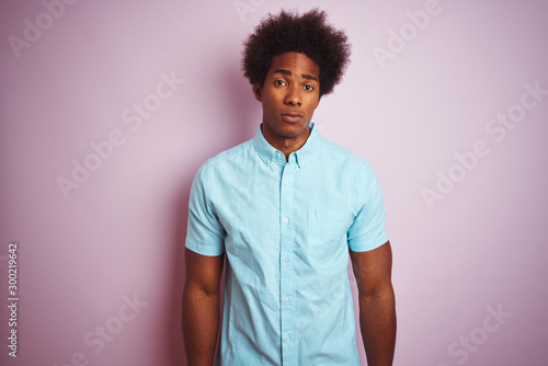 Young american man with afro hair wearing blue shirt standing over isolated pink background Relaxed with serious expression on face. Simple and natural looking at the camera.