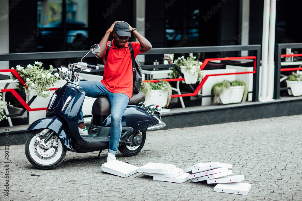 Dissatisfied male brings best food of his restaurant, delivers pizza in cardboard boxes, has tired facial expression, uses fast motorbike to distribute fast food for customers.