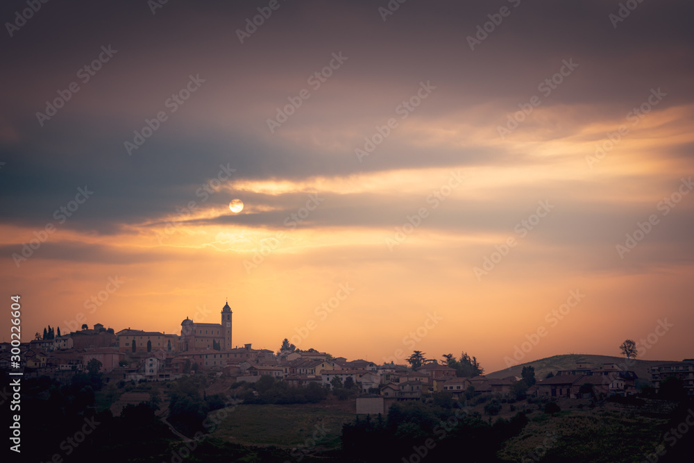 Beautiful Italian landscape with rolling hills, silhouette of old castle, vineyards and dramatic clouds at sunrise. Warm tones
