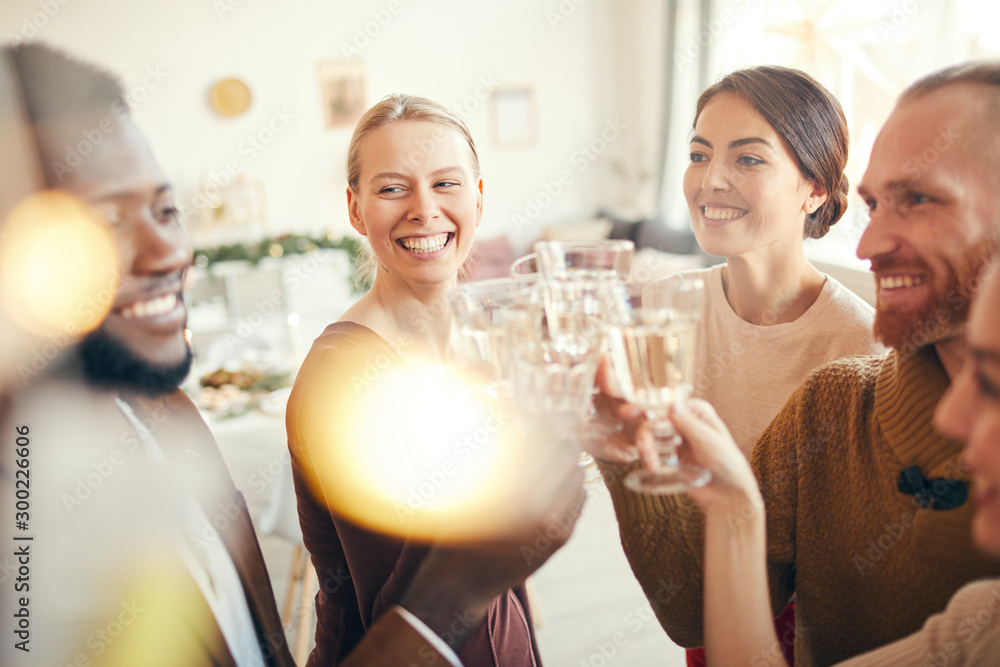 Elegant group of friends raising glasses while celebrating at Christmas party, focus on two women smiling cheerfully