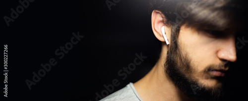 Close-up portrait of young hipster with earbuds, on black background.