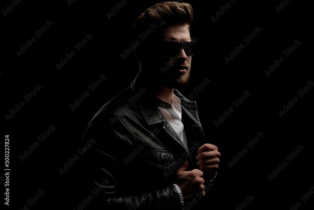 man wearing sunglasses standing in the shadow grabbing his jacket