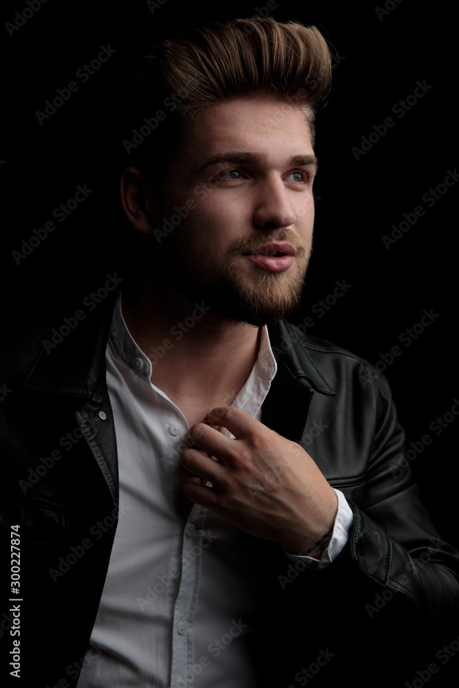 casual man wearing leather jacket fixing collar and looking away