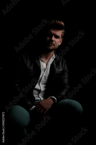 casual man wearing leather jacket sitting in the shadows