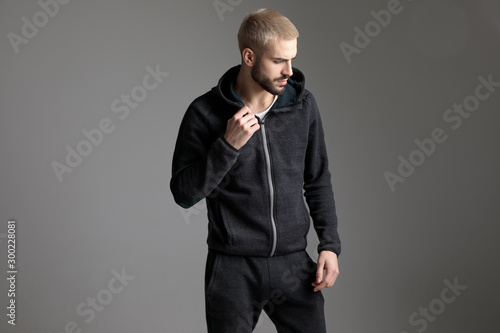 Fotografie casual man standing and fixing his tracksuit while looking aside
