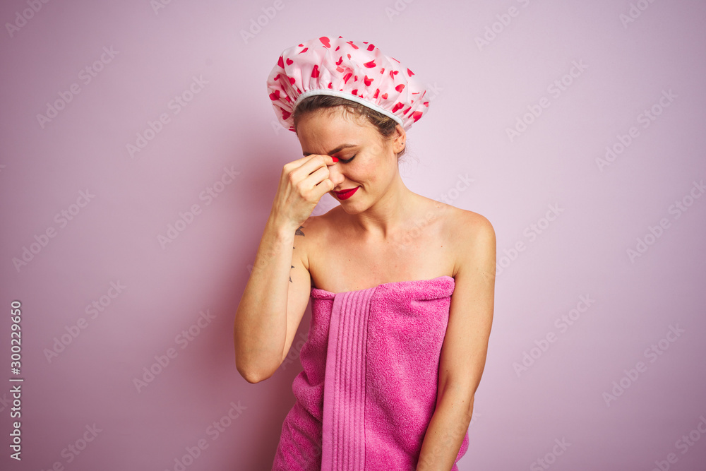 Young beautiful woman wearing towel and bath hat after shower over pink isolated background tired rubbing nose and eyes feeling fatigue and headache. Stress and frustration concept.
