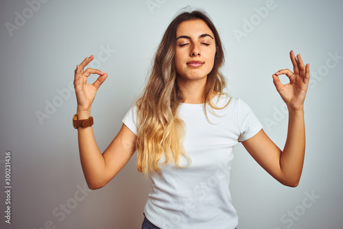 Young beautiful woman wearing casual white t-shirt over isolated background relaxed and smiling with eyes closed doing meditation gesture with fingers. Yoga concept.