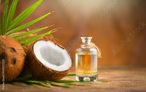 Coconut palm oil in a bottle with coconuts and green palm tree leaf on brown background. Coco nut closeup. Healthy Food, skin care concept. Vegan food. Skincare treatments. Aromatherapy