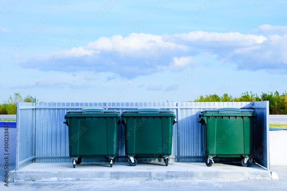 Green trash containers outdoors on a background of sky and trees. Green trash containers outdoors on a background of sky and trees.