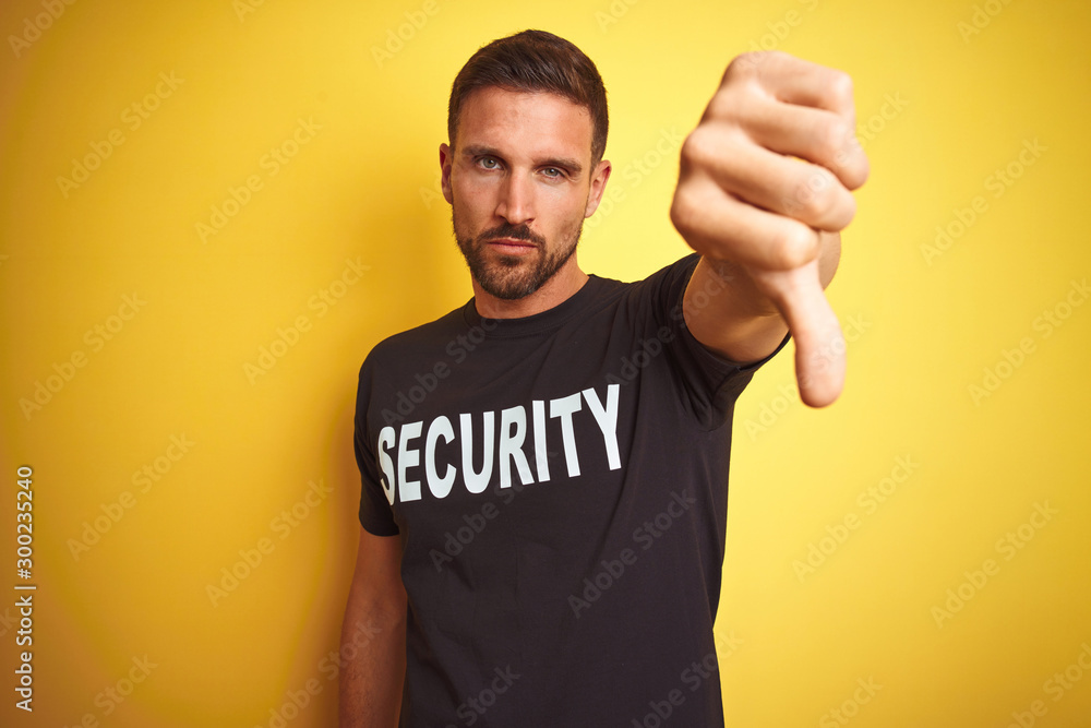 Young safeguard man wearing security uniform over yellow isolated background looking unhappy and angry showing rejection and negative with thumbs down gesture. Bad expression. Young safeguard man wearing security uniform over yellow isolated background looking unhappy and angry showing rejection and negative with thumbs down gesture. Bad expression.