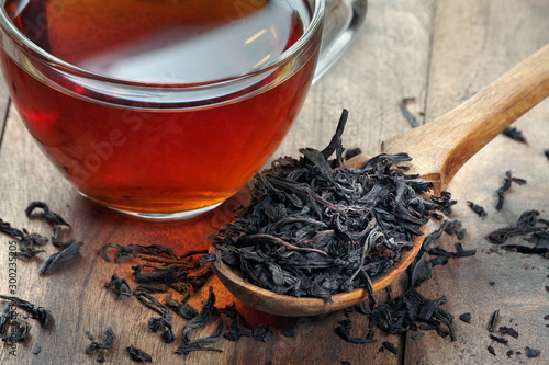 dry leaves of black tea in a wooden spoon. a cup of freshly brewed tea.