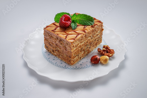 Cake piece with nuts, chocolate, mint and raspberry on a plate isolated on white background