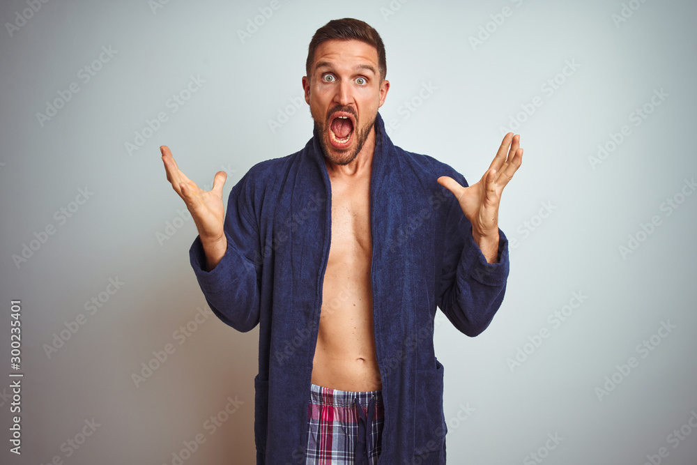 Naklejka premium Sexy shirtless man wearing comfortable pajamas and robe over isolated background celebrating crazy and amazed for success with arms raised and open eyes screaming excited. Winner concept