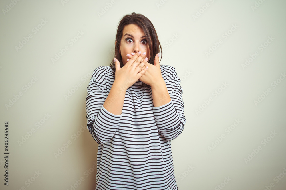 Young beautiful brunette woman wearing striped sweater over white isolated background shocked covering mouth with hands for mistake. Secret concept. Young beautiful brunette woman wearing striped sweater over white isolated background shocked covering mouth with hands for mistake. Secret concept.