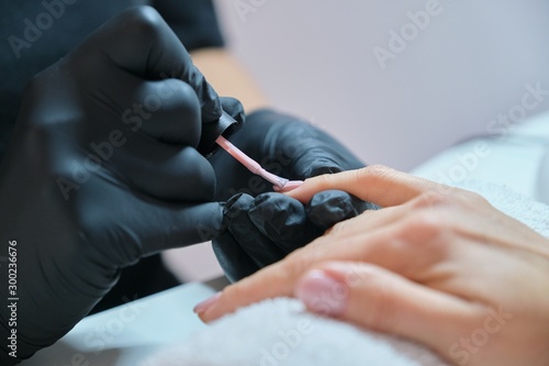Manicurist varnishes gel nails. Professional hand and nail care in beauty salon