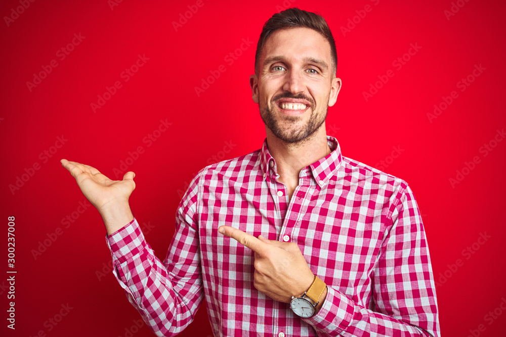 Young handsome man over red isolated background amazed and smiling to the camera while presenting with hand and pointing with finger. Young handsome man over red isolated background amazed and smiling to the camera while presenting with hand and pointing with finger.