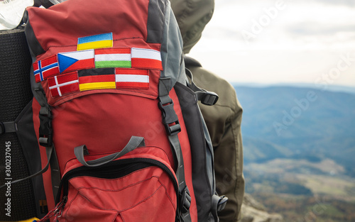 travel and hiking life style photography concept picture of different European countries flag stripes on backpack in mountains route environment with blurred background copy space for your text here 