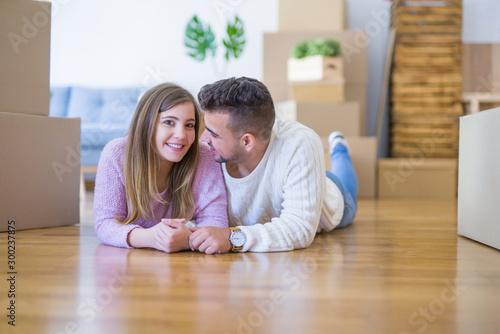 Young beautiful couple in love moving to new home, lying on the floor around cardboard boxes, very happy and cheerful for new apartment