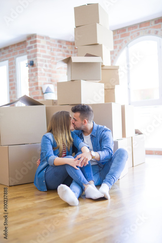 Young beautiful couple in love moving to new home, sitting on the floor very happy and cheerful for new apartment around cardboard boxes