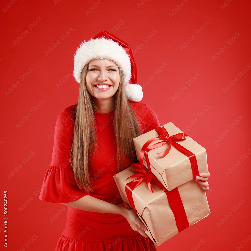 Happy young woman in Santa hat with Christmas gifts on red background Happy young woman in Santa hat with Christmas gifts on red background
