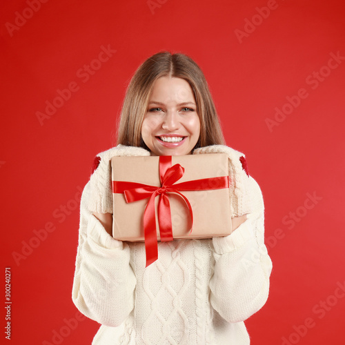 Happy young woman with Christmas gift on red background