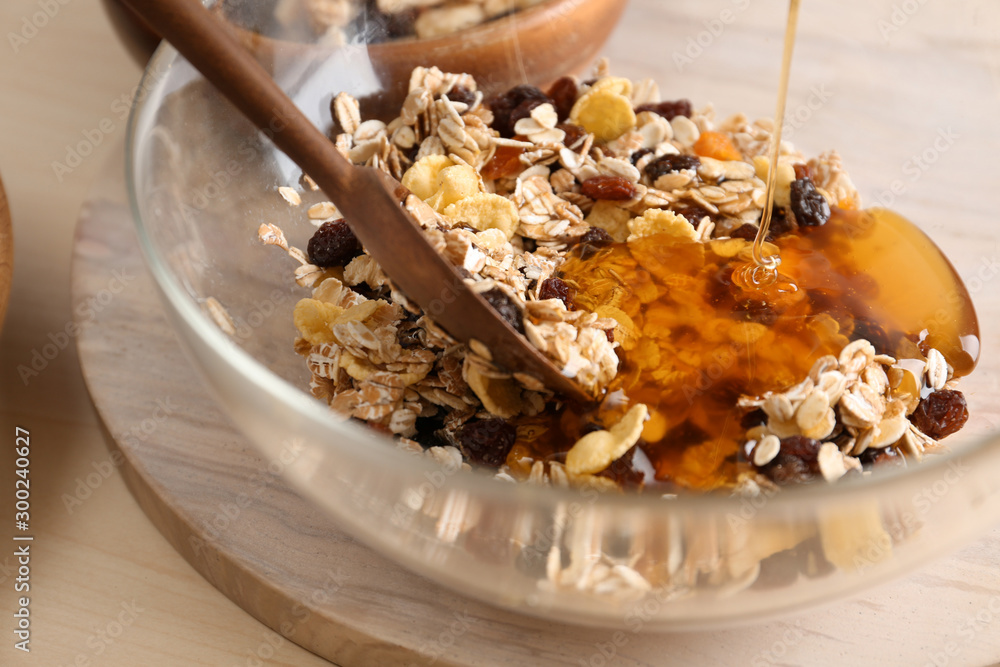 Pouring honey into bowl with oatmeal flakes and raisins on table, closeup. Healthy granola bar preparation Pouring honey into bowl with oatmeal flakes and raisins on table, closeup. Healthy granola bar preparation