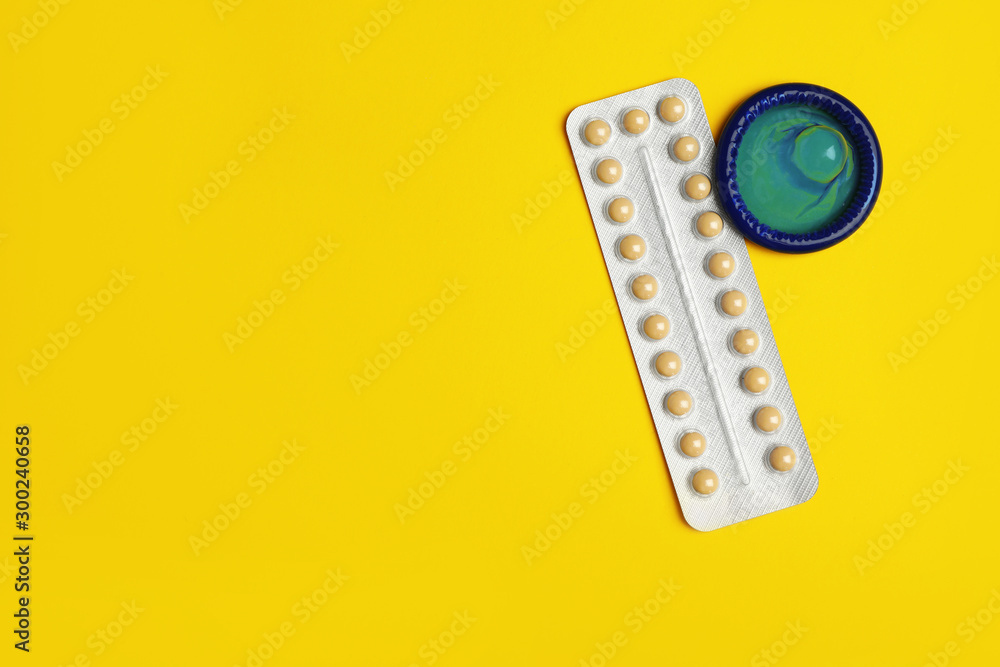Condom and birth control pills on yellow background, flat lay with space for text. Safe sex concept Condom and birth control pills on yellow background, flat lay with space for text. Safe sex concept