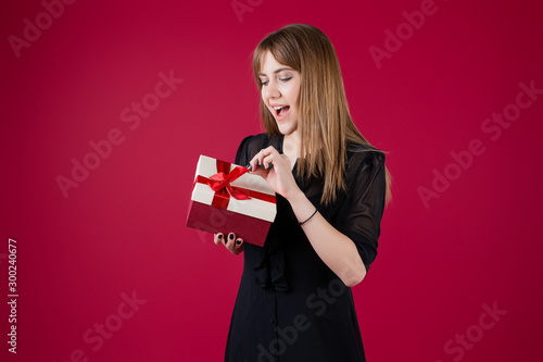 woman holding gift box with red ribbon wearing dress isolated over red