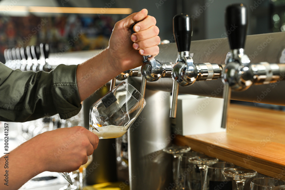 Bartender pouring fresh beer into glass in pub, closeup