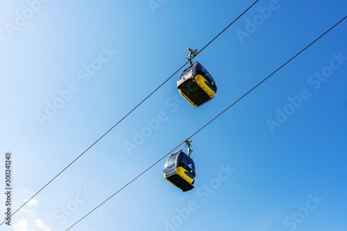 Cable car cabins liftng up on mountain against blue sky.