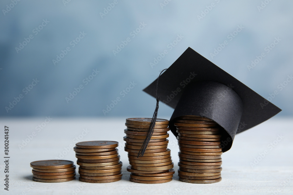 Coins and student graduation hat on white wooden table against blue  background. Tuition fees concept Stock Photo | Adobe Stock