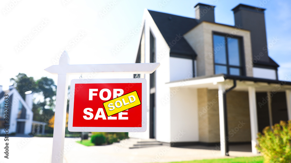 Red real estate sign near house outdoors on sunny day Red real estate sign near house outdoors on sunny day