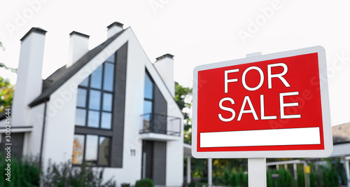 Red real estate sign near house outdoors on sunny day