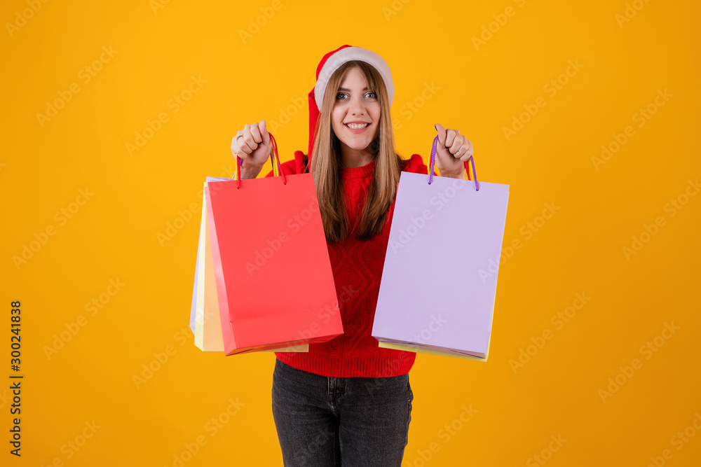 excited woman with gifts in holiday shopping bags wearing santa hat and sweater isolated over yellow excited woman with gifts in holiday shopping bags wearing santa hat and sweater isolated over yellow