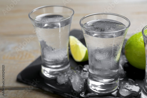 Shots of vodka, lime and ice on wooden table