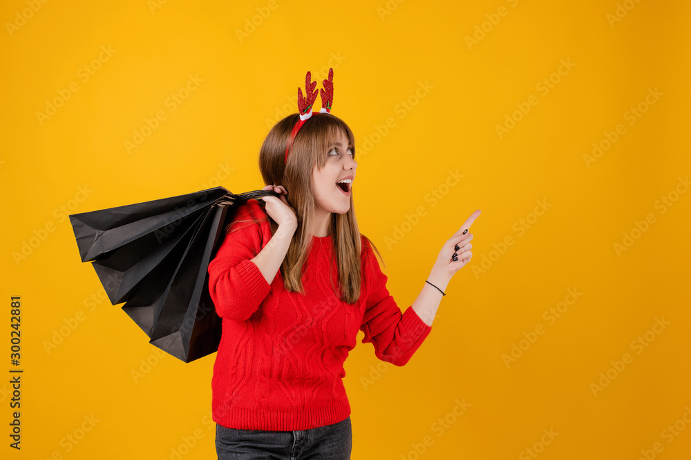 happy girl with gifts in holiday shopping bags pointing at copy space wearing funny hoop isolated over yellow happy girl with gifts in holiday shopping bags pointing at copy space wearing funny hoop isolated over yellow