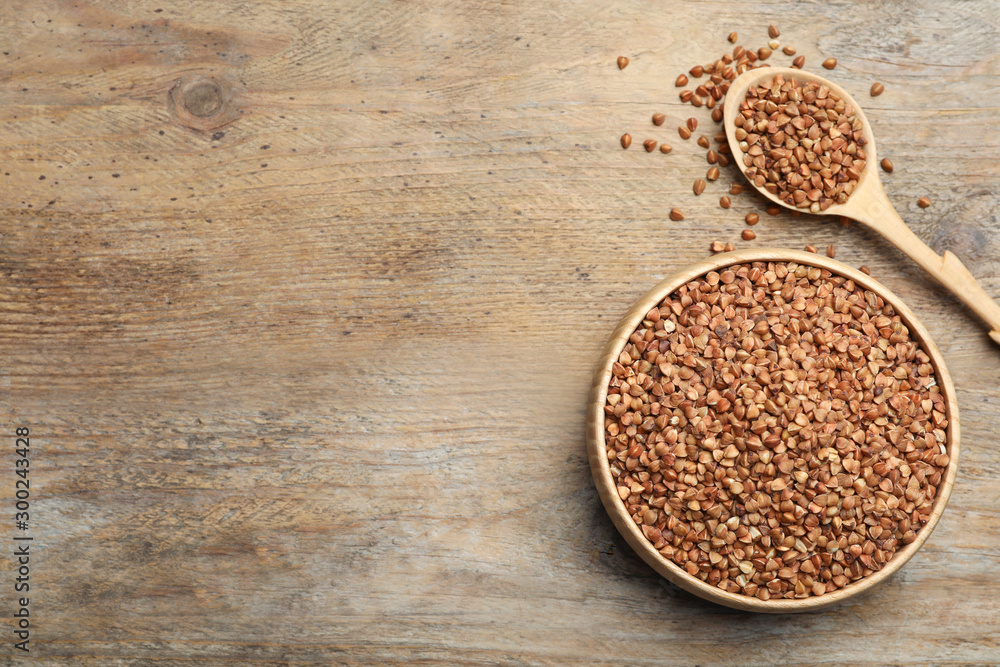 Bowl and spoon of uncooked buckwheat on wooden table, flat lay. Space for text Bowl and spoon of uncooked buckwheat on wooden table, flat lay. Space for text