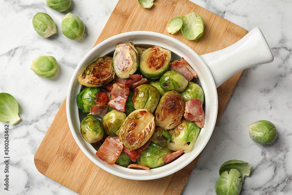 Delicious Brussels sprouts with bacon in dish on white marble table, flat lay Delicious Brussels sprouts with bacon in dish on white marble table, flat lay