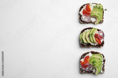 Delicious avocado sandwiches on white table, flat lay. Space for text