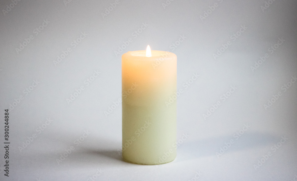 a white candle stands on a gray background, a fire burns a white candle stands on a gray background, a fire burns