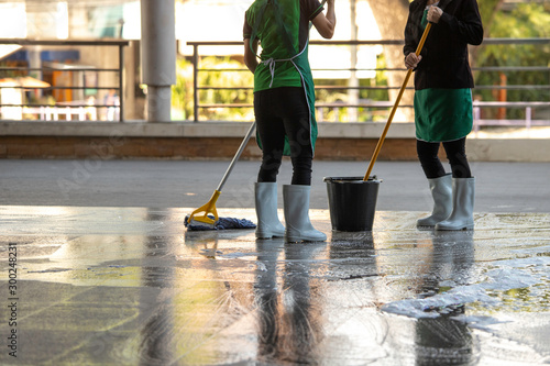 cleaner with mop and uniform cleaning hall floor of public business building