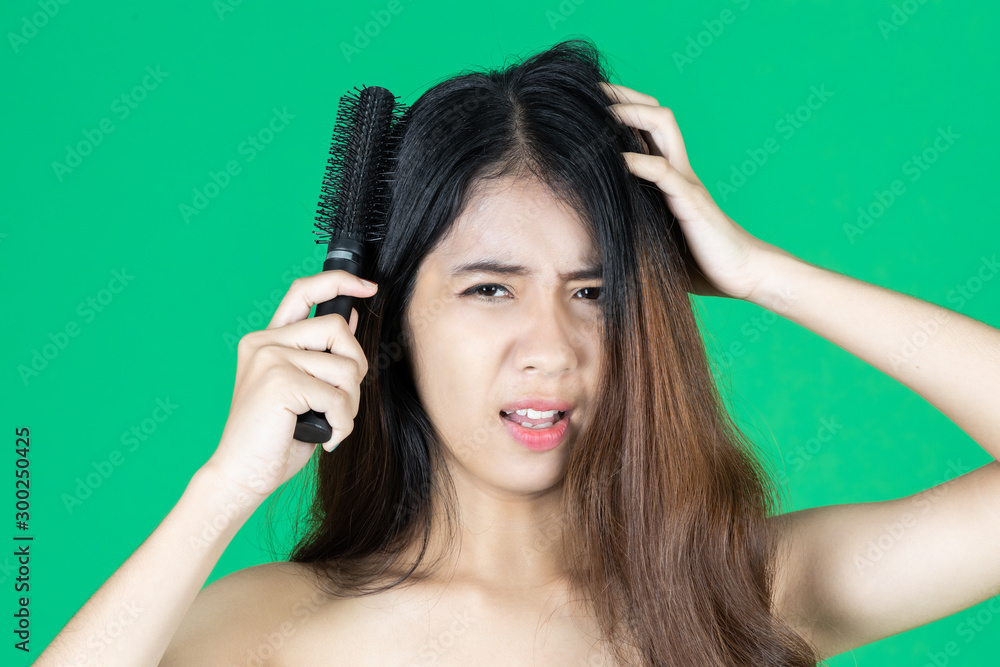 Fototapeta premium Upset stressed young Asian woman holding damaged dry hair on hands over green isolated background.