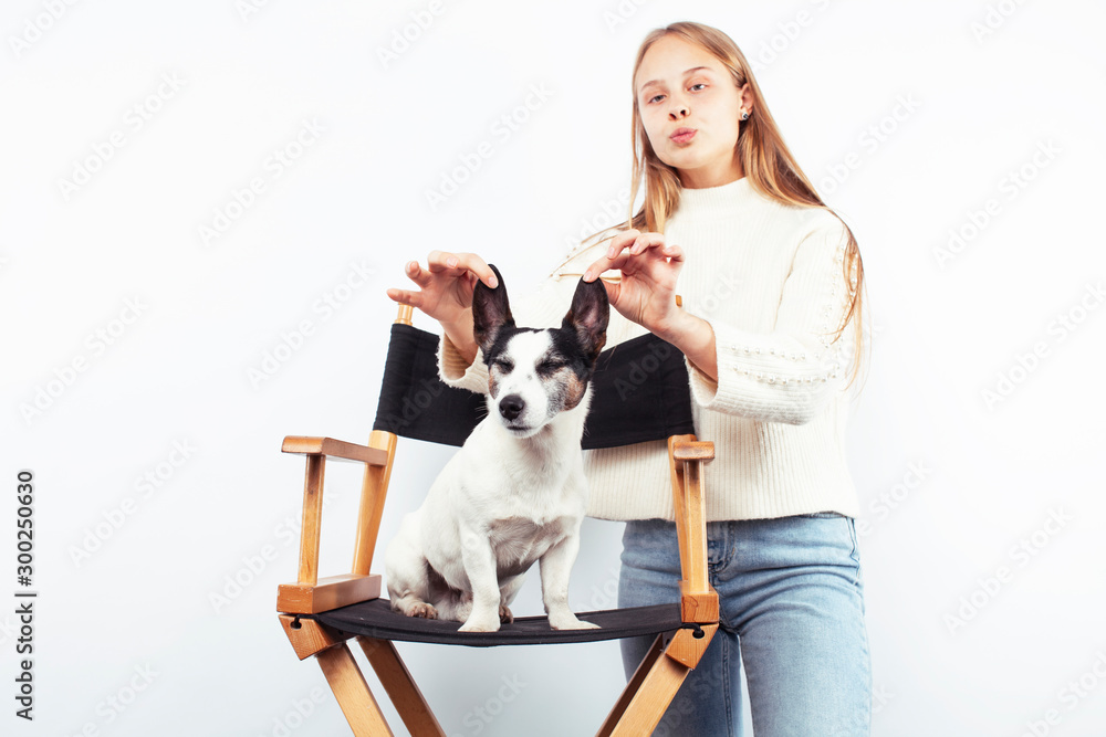 cute blond teenage girl making funny faces playing with her little dog in chair isolated on white background, lifestyle people concept