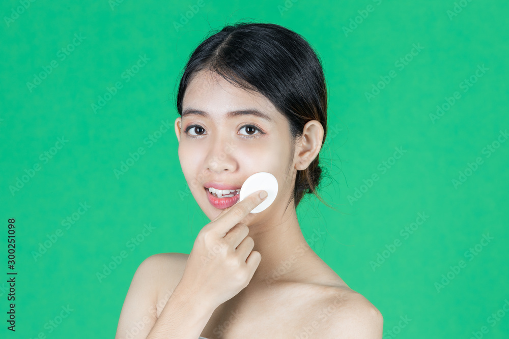 Pretty beauty young Asian woman cleaning her face with cotton pad over green isolated background. Healthy skin and cosmetics concept. Pretty beauty young Asian woman cleaning her face with cotton pad over green isolated background. Healthy skin and cosmetics concept.