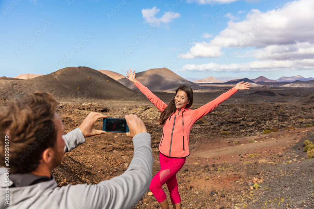 Tourists taking picture vlogging outside on Europe travel, girl posing for boyfriend with arms up having fun on Timanfaya National Park, Lanzarote, Canary Islands. - obrazy, fototapety, plakaty 