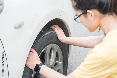 Cropped shot of young woman touching and checking her car tyre. She worrying about somethings wrong with her wheel.